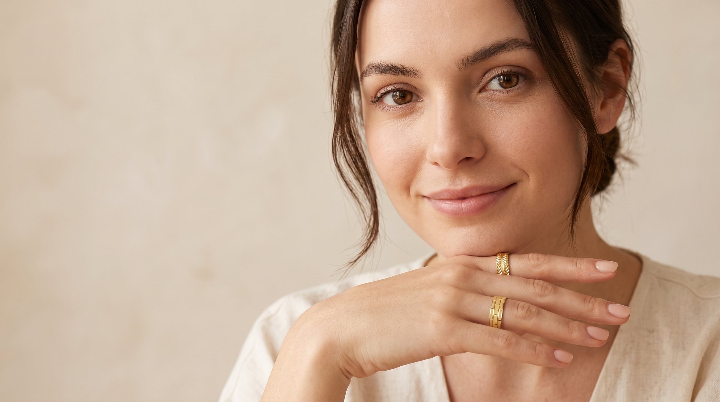 A woman resting her chin on her hand, wearing two S.N.K gold rings